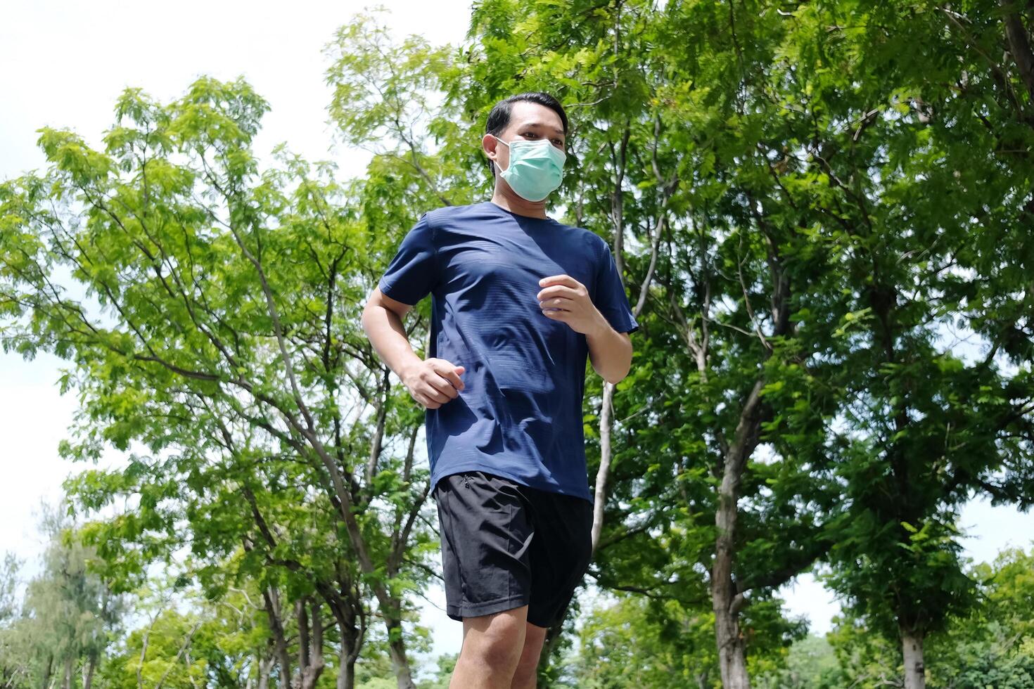 Asian young man is wearing face mask for prevent Covid19 virus and running in the garden. Healthcare and exercise Concept photo