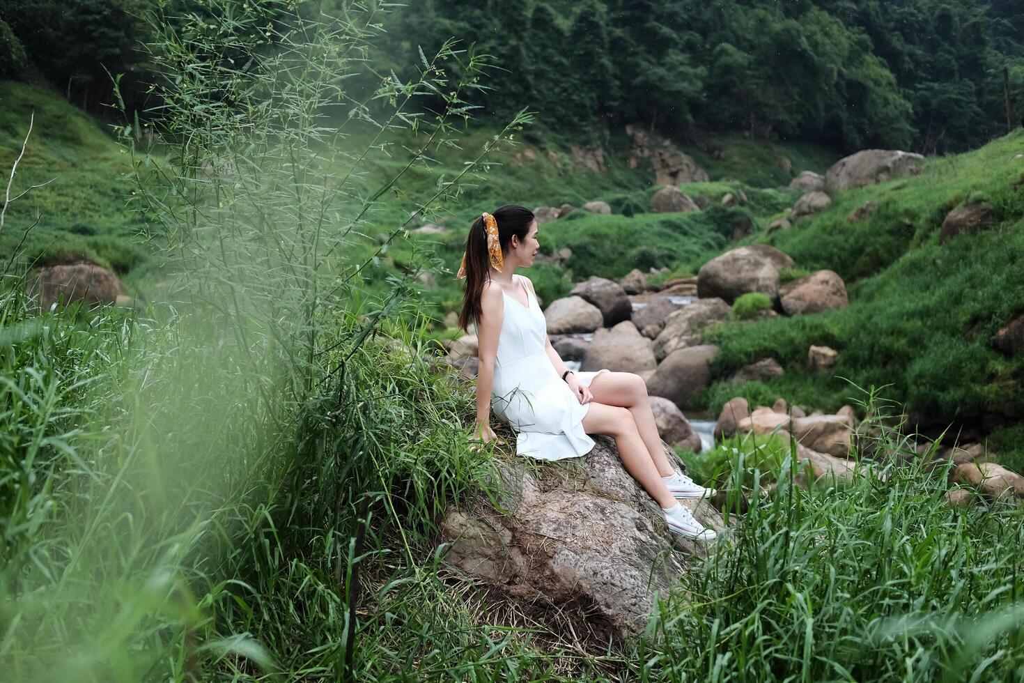Asian woman wear white dress is sitting on the rock in forest. Freedom in the nature concept photo