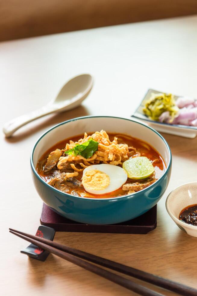Northern Thai style curried noodle soup with beef and egg on wooden table photo