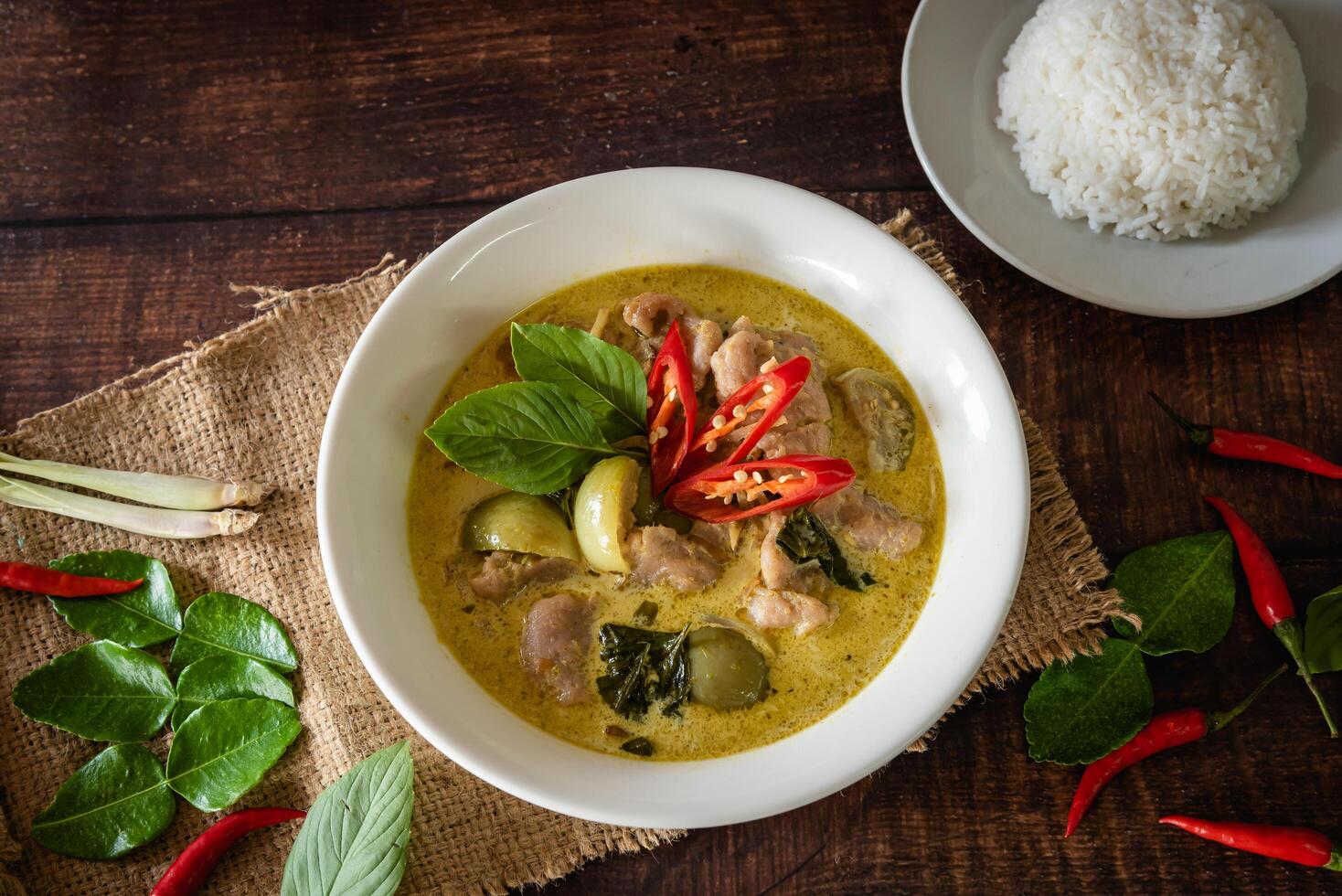 Traditional Thai chicken green curry with fresh vegetable and herb in bowl on wooden table, serve with steamed rice photo
