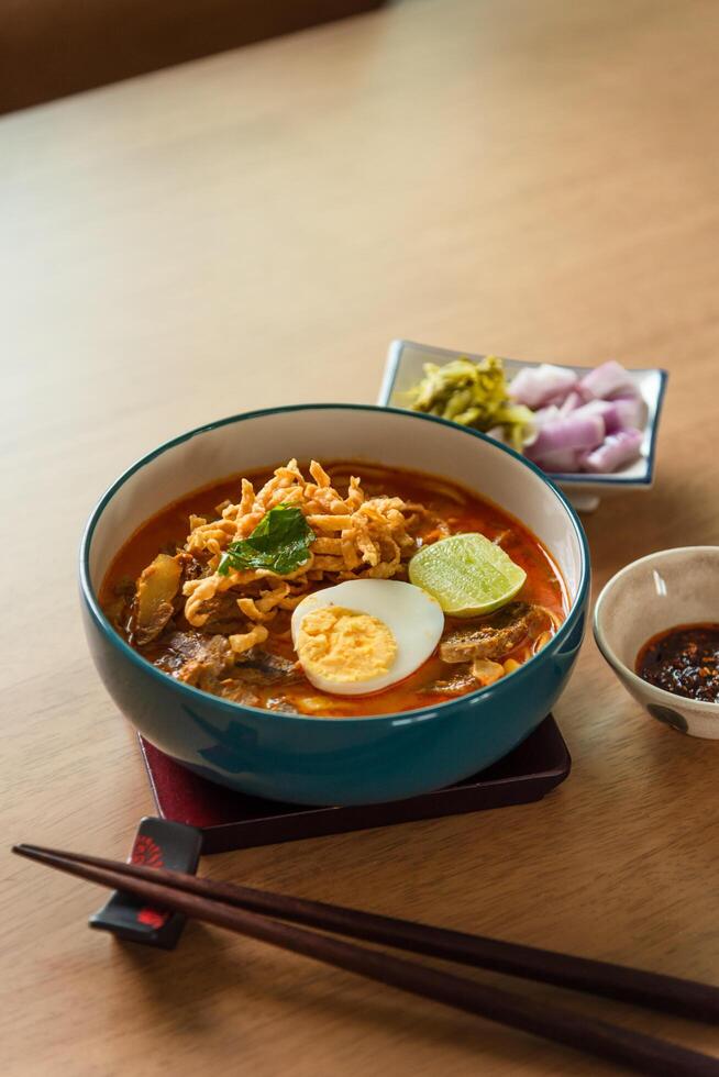 Northern Thai style curried noodle soup with beef and egg on wooden table photo