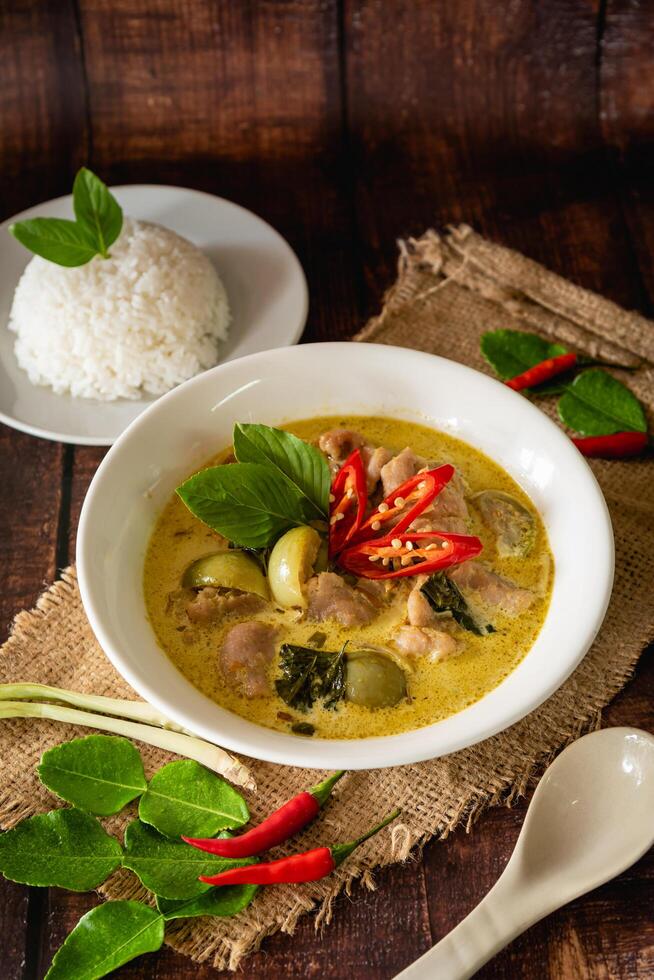 Traditional Thai chicken green curry with fresh vegetable and herb in bowl on wooden table, serve with steamed rice photo