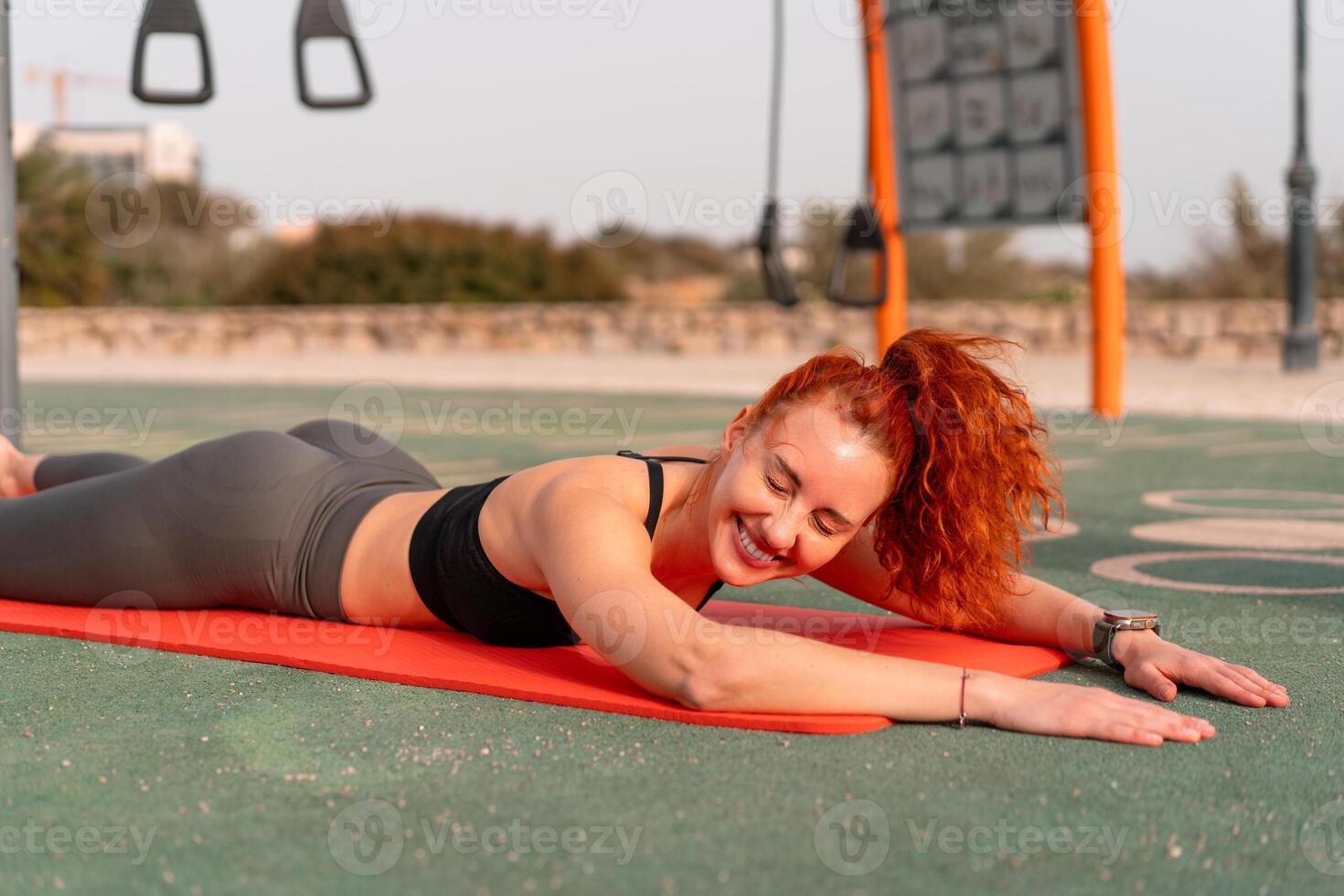 Smiling redhead woman lying on yoga mat at summer park photo