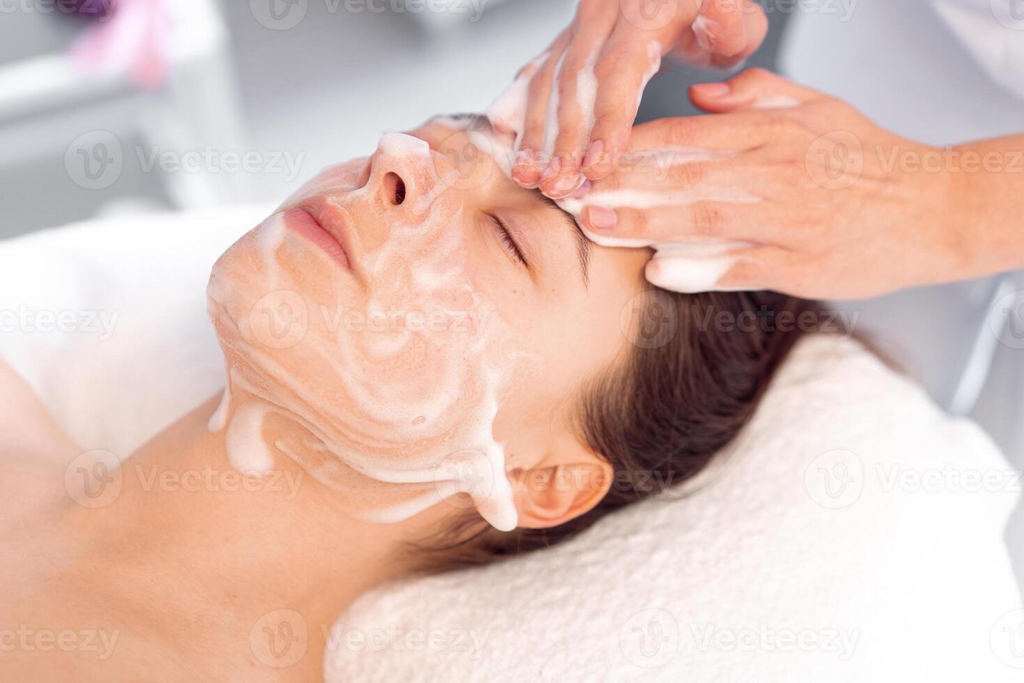 Cosmetologist cleanses the skin of woman with foam in clinic photo