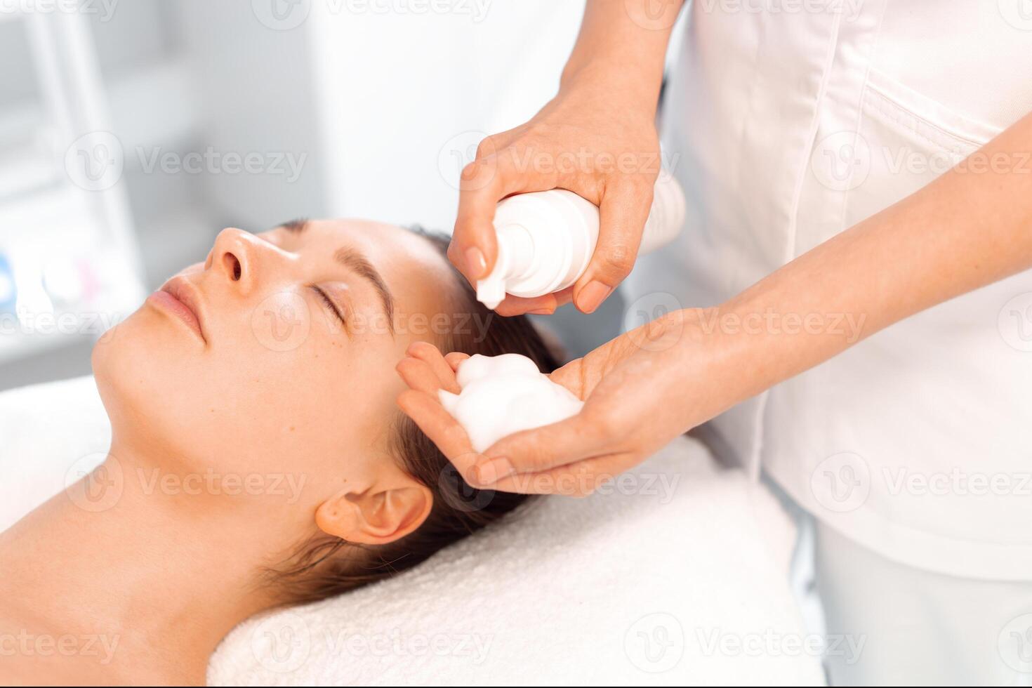 Esthetician preparing to apply cleansing foam on face of woman photo