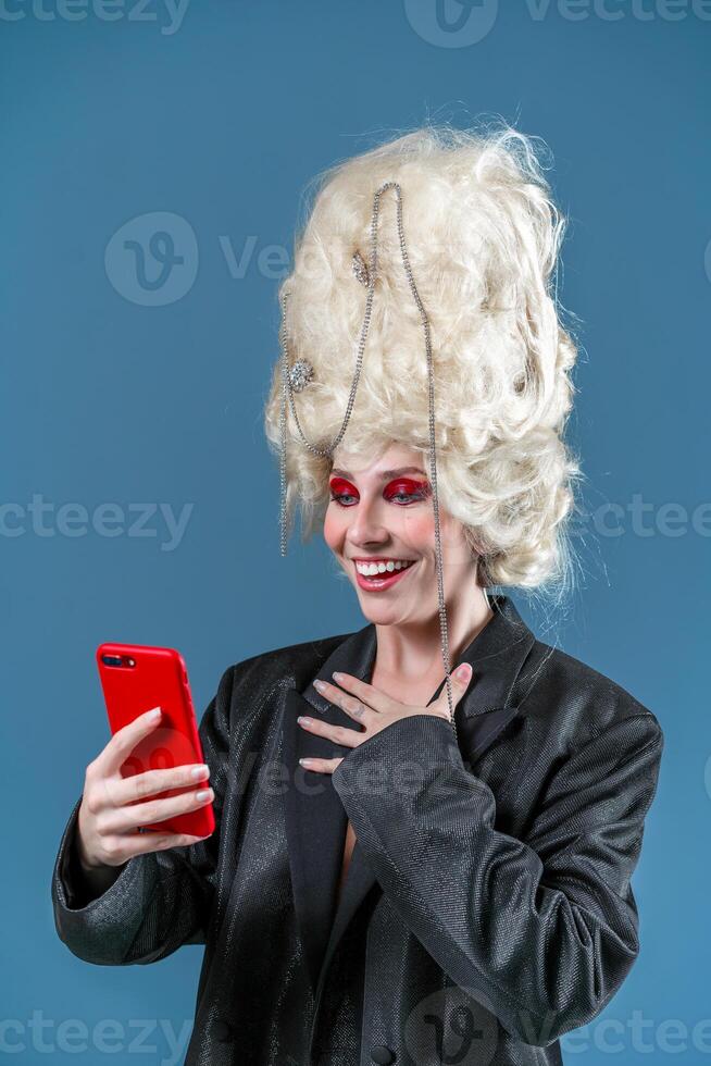 Happy surprised woman in wig using smartphone in blue studio photo