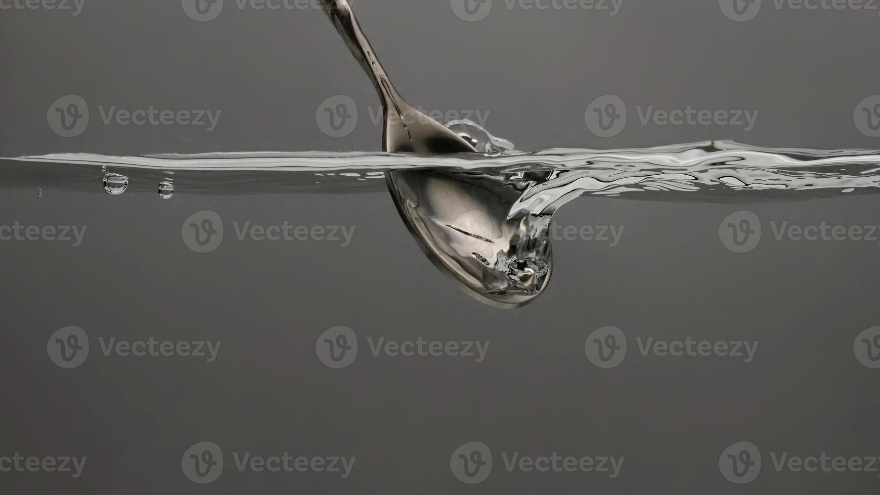 Stirring drinks by bar spoon. Underwater of silver metal bar spoon stir clear alcoholic drinks such as Vodka Gin or Tequila close up shot. Bartender spoon under clear water against grey background. photo