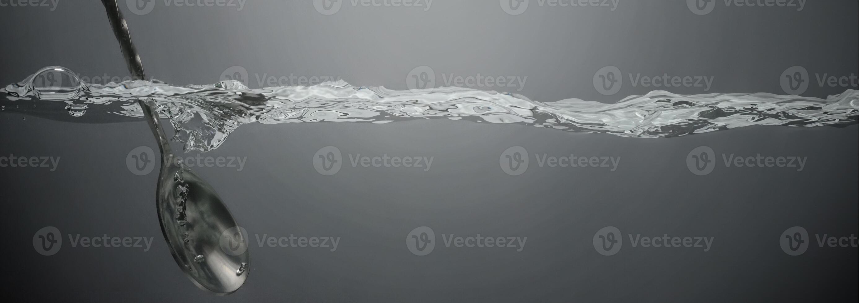 Stirring drinks by bar spoon. Underwater of silver metal bar spoon stir clear alcoholic drinks such as Vodka Gin or Tequila close up shot. Bartender spoon under clear water against grey background. photo