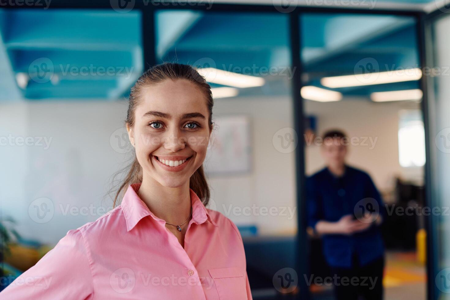 Portrait of young smiling business woman in creative open space coworking startup office. Successful businesswoman standing in office with copyspace. Coworkers working in background photo