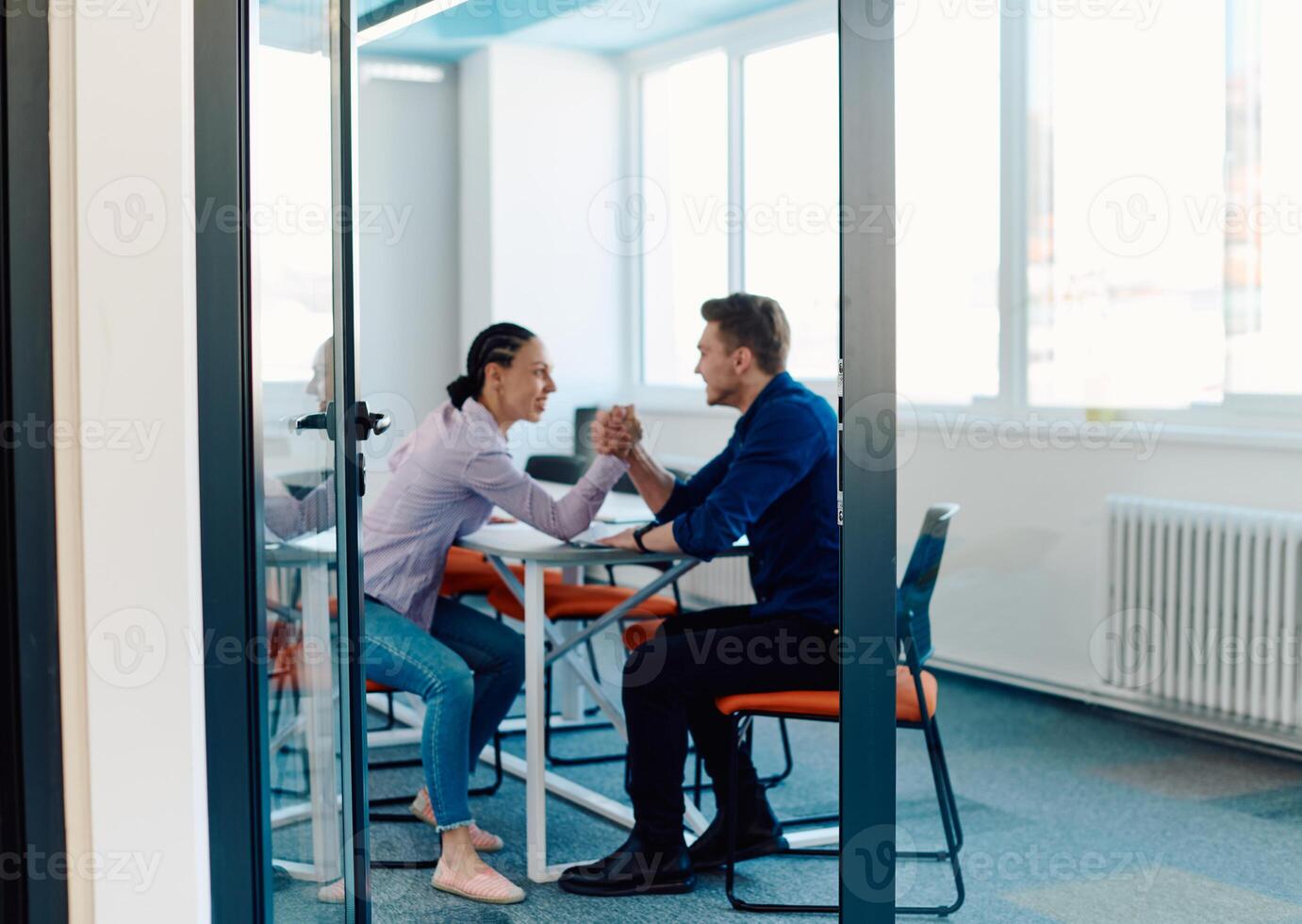In a modern startup office, a businessman and a businesswoman business colleagues engage in a symbolic arm-wrestling match, reflecting teamwork, competition, and innovation in their dynamic workplace. photo