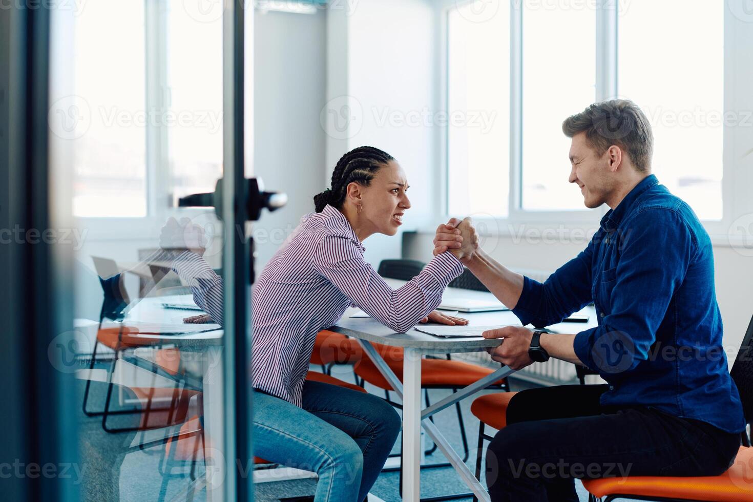 In a modern startup office, a businessman and a businesswoman business colleagues engage in a symbolic arm-wrestling match, reflecting teamwork, competition, and innovation in their dynamic workplace. photo