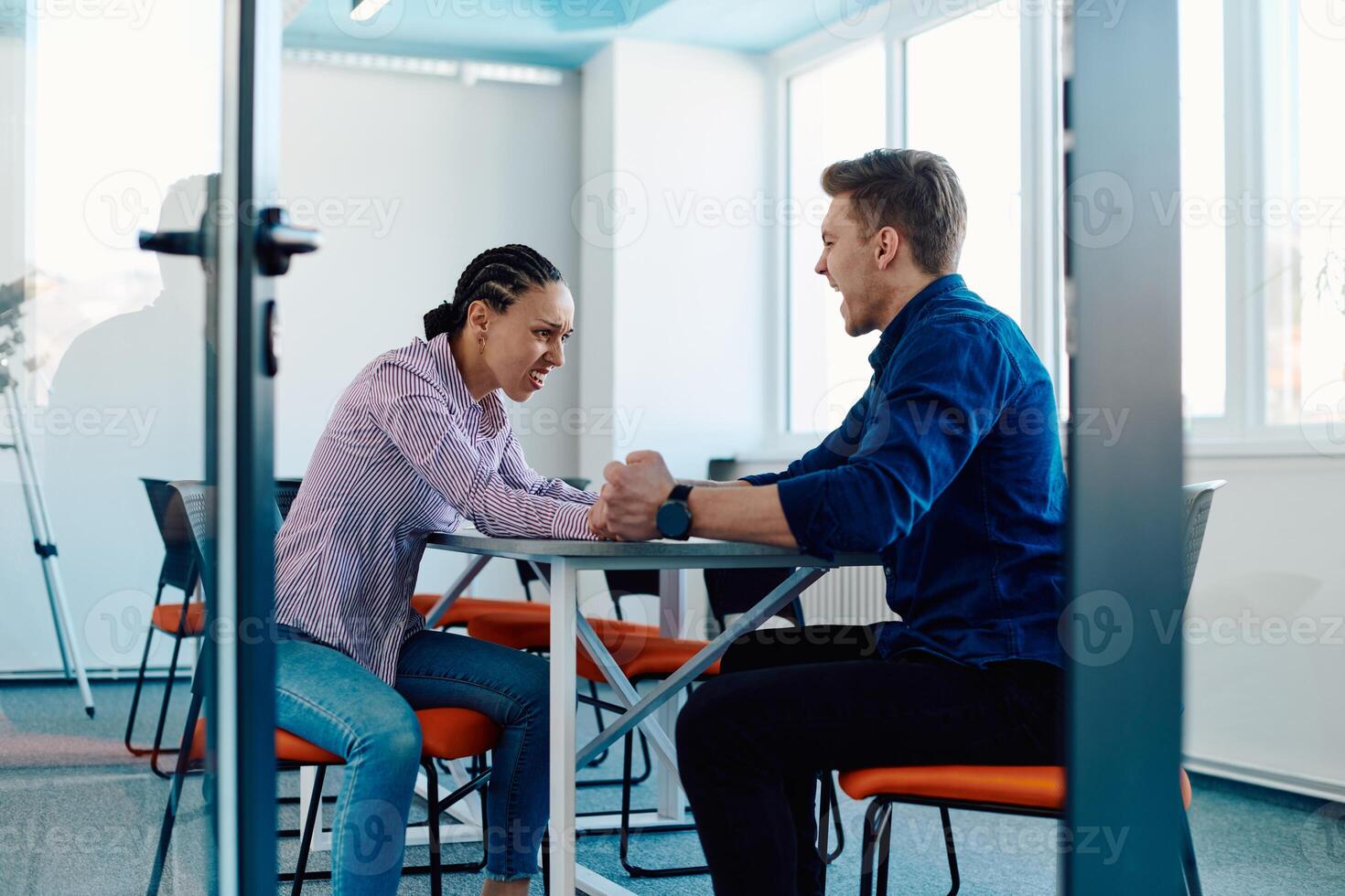 In a modern startup office, a businessman and a businesswoman business colleagues engage in a symbolic arm-wrestling match, reflecting teamwork, competition, and innovation in their dynamic workplace. photo
