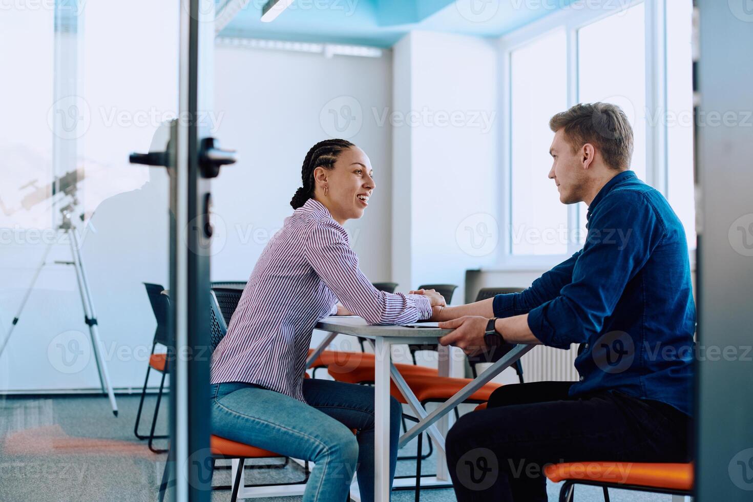 In a modern startup office, a businessman and a businesswoman business colleagues engage in a symbolic arm-wrestling match, reflecting teamwork, competition, and innovation in their dynamic workplace. photo