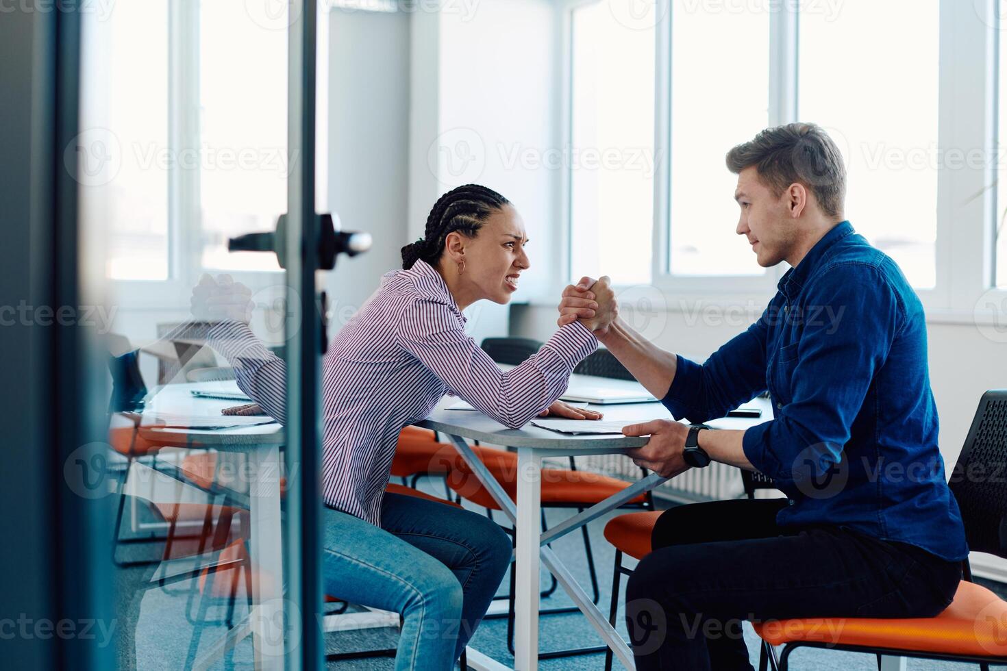 In a modern startup office, a businessman and a businesswoman business colleagues engage in a symbolic arm-wrestling match, reflecting teamwork, competition, and innovation in their dynamic workplace. photo
