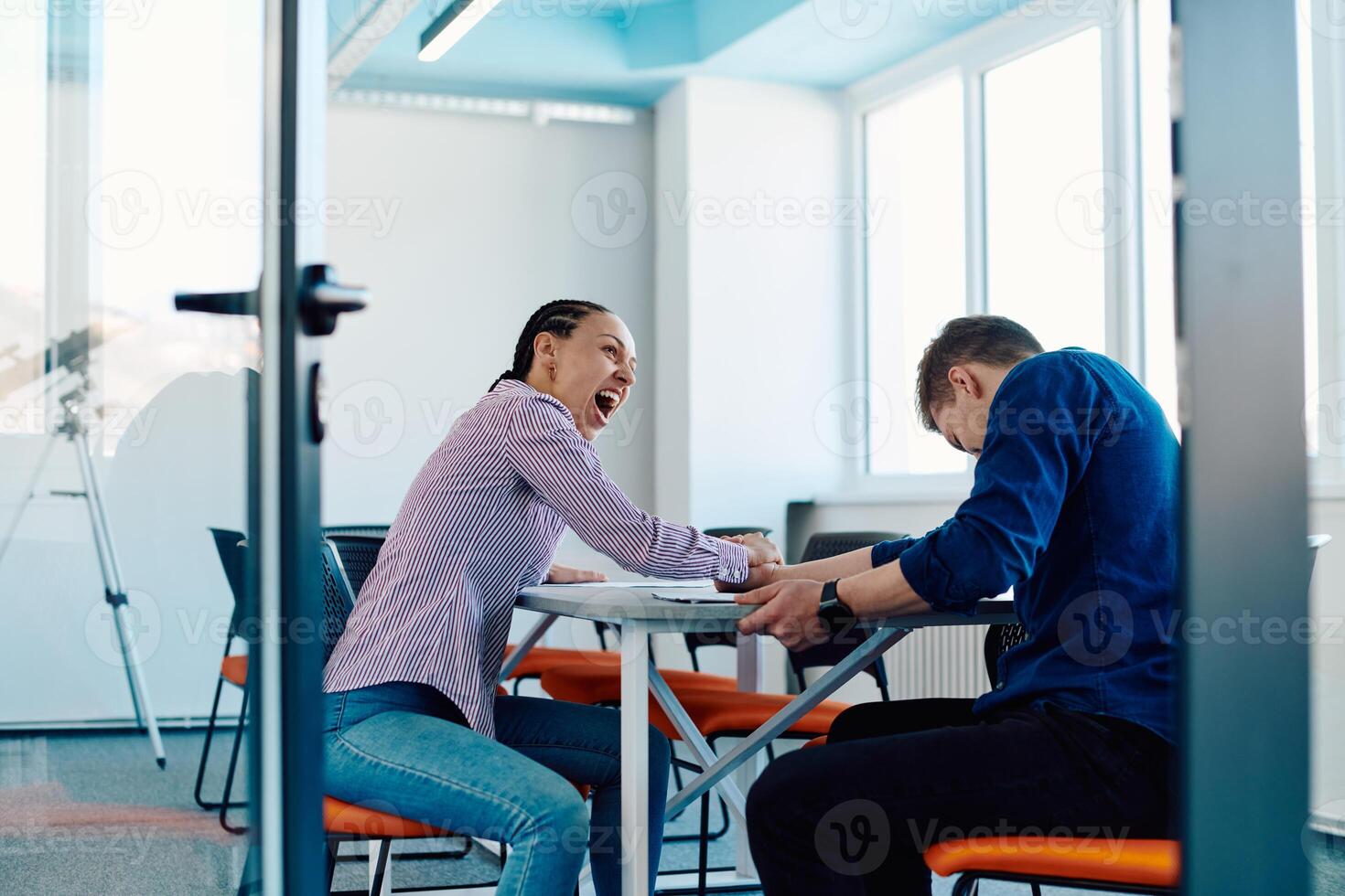 In a modern startup office, a businessman and a businesswoman business colleagues engage in a symbolic arm-wrestling match, reflecting teamwork, competition, and innovation in their dynamic workplace. photo