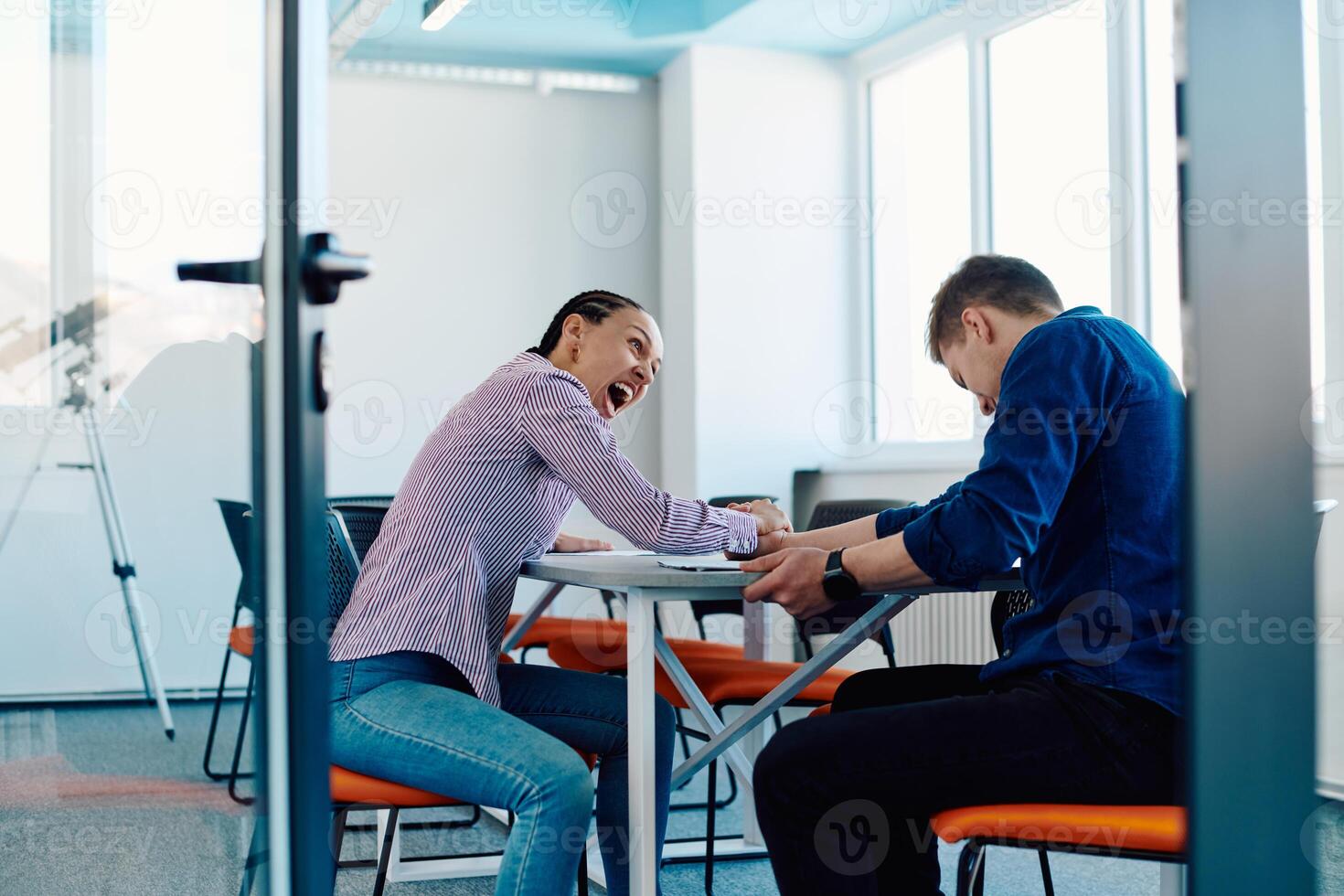 In a modern startup office, a businessman and a businesswoman business colleagues engage in a symbolic arm-wrestling match, reflecting teamwork, competition, and innovation in their dynamic workplace. photo