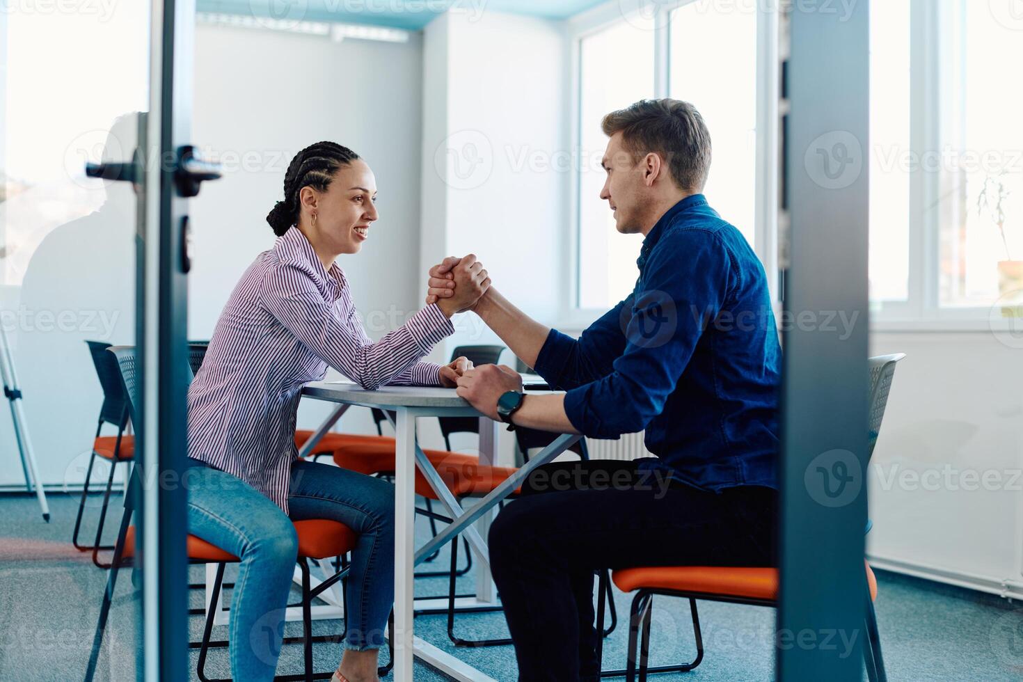 In a modern startup office, a businessman and a businesswoman business colleagues engage in a symbolic arm-wrestling match, reflecting teamwork, competition, and innovation in their dynamic workplace. photo