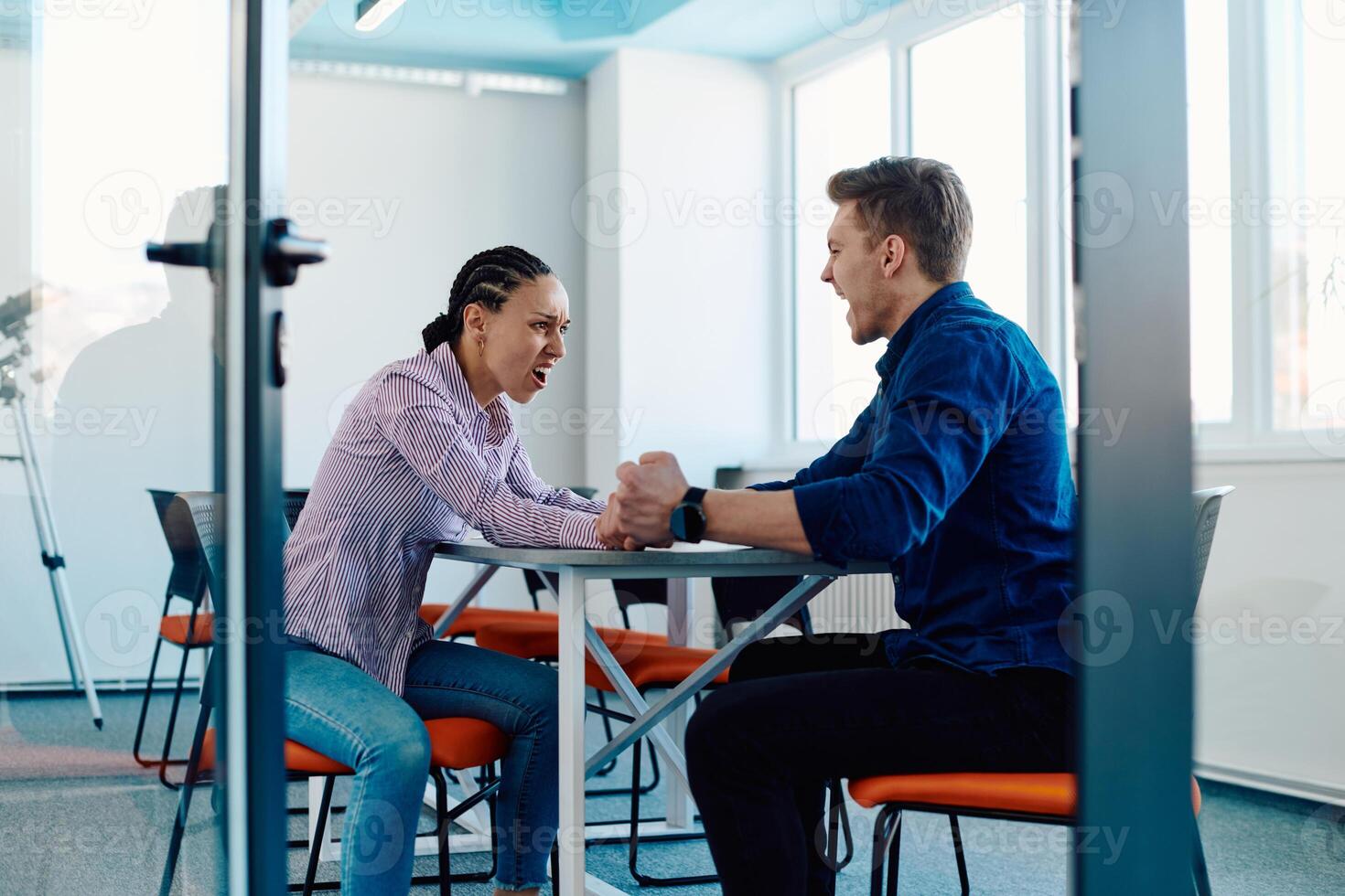 In a modern startup office, a businessman and a businesswoman business colleagues engage in a symbolic arm-wrestling match, reflecting teamwork, competition, and innovation in their dynamic workplace. photo