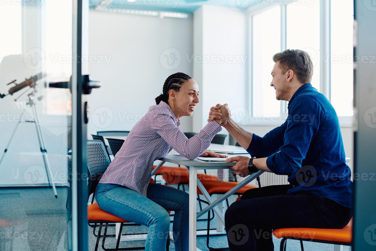 In a modern startup office, a businessman and a businesswoman business colleagues engage in a symbolic arm-wrestling match, reflecting teamwork, competition, and innovation in their dynamic workplace. photo