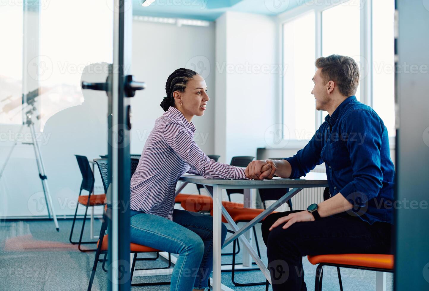 In a modern startup office, a businessman and a businesswoman business colleagues engage in a symbolic arm-wrestling match, reflecting teamwork, competition, and innovation in their dynamic workplace. photo
