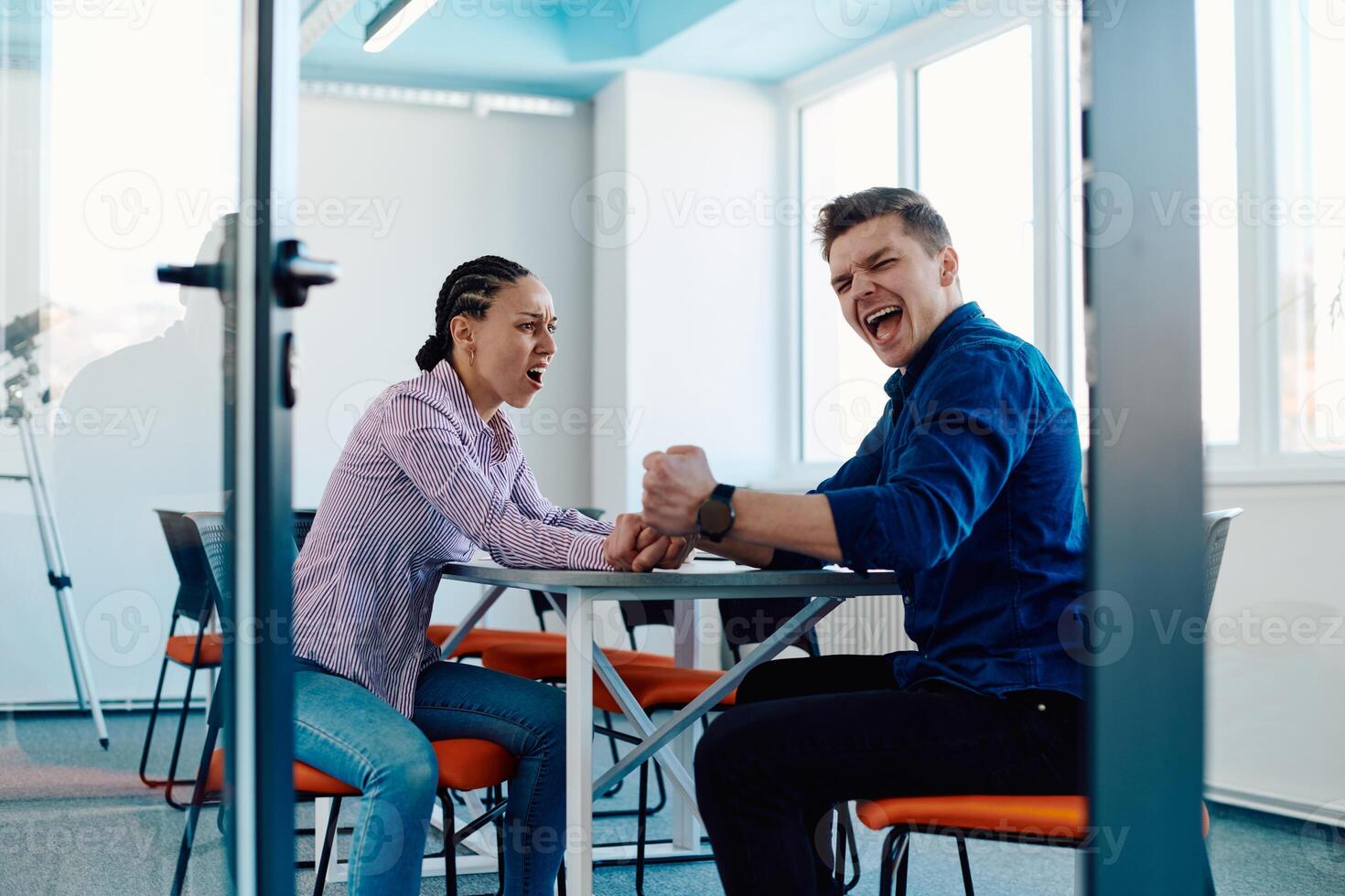 In a modern startup office, a businessman and a businesswoman business colleagues engage in a symbolic arm-wrestling match, reflecting teamwork, competition, and innovation in their dynamic workplace. photo