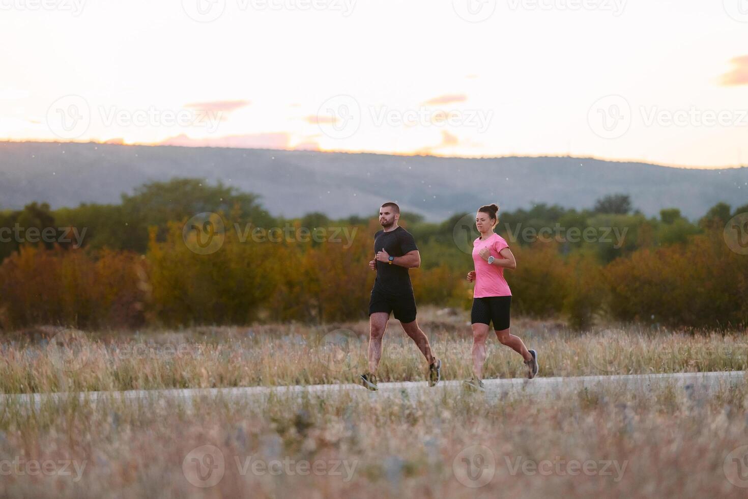 A couple dressed in sportswear runs along a scenic road during an early morning workout, enjoying the fresh air and maintaining a healthy lifestyle photo
