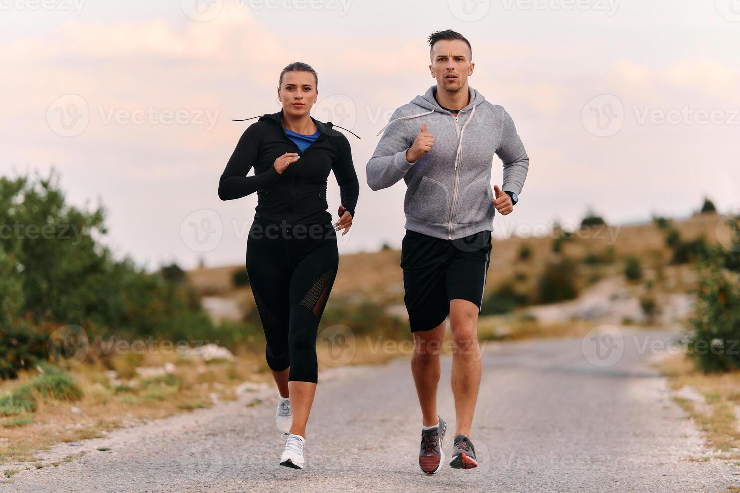 A couple dressed in sportswear runs along a scenic road during an early morning workout, enjoying the fresh air and maintaining a healthy lifestyle photo