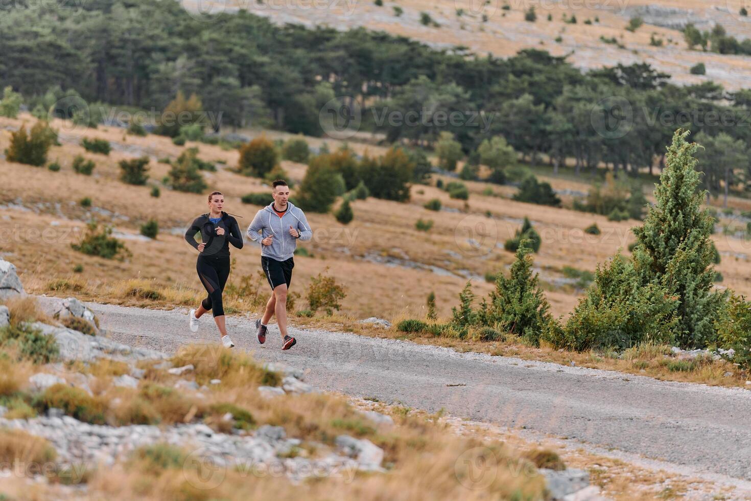A couple dressed in sportswear runs along a scenic road during an early morning workout, enjoying the fresh air and maintaining a healthy lifestyle photo