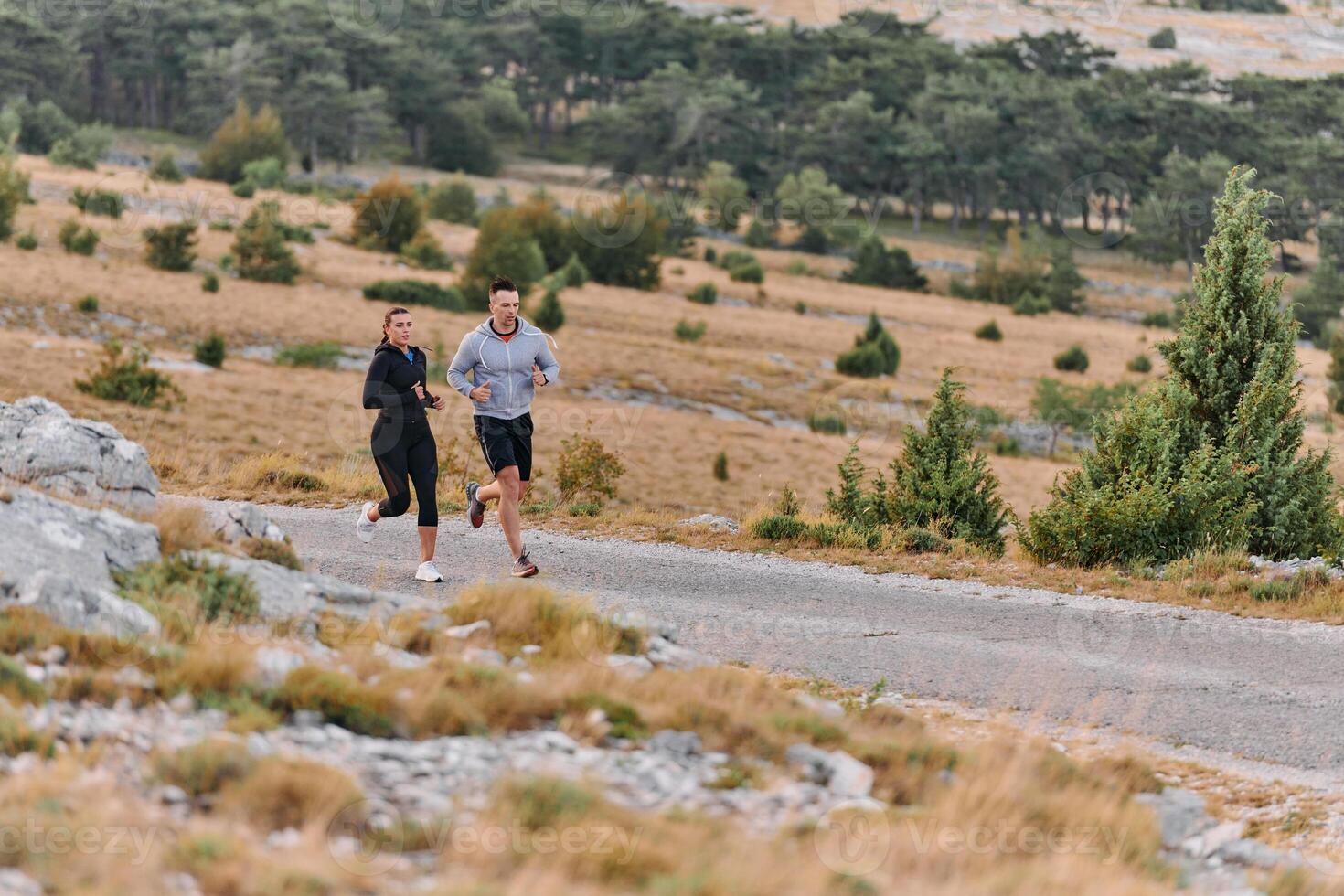 A couple dressed in sportswear runs along a scenic road during an early morning workout, enjoying the fresh air and maintaining a healthy lifestyle photo