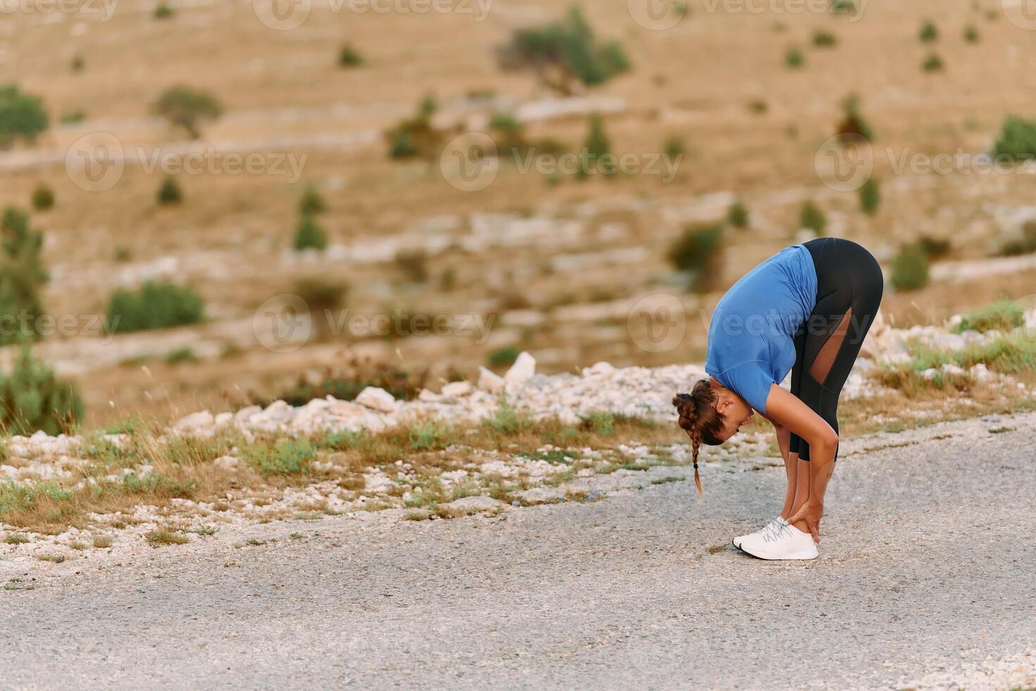 Determined Female Athlete Stretching After an Intense Run Through Rugged Mountain Terrain. photo