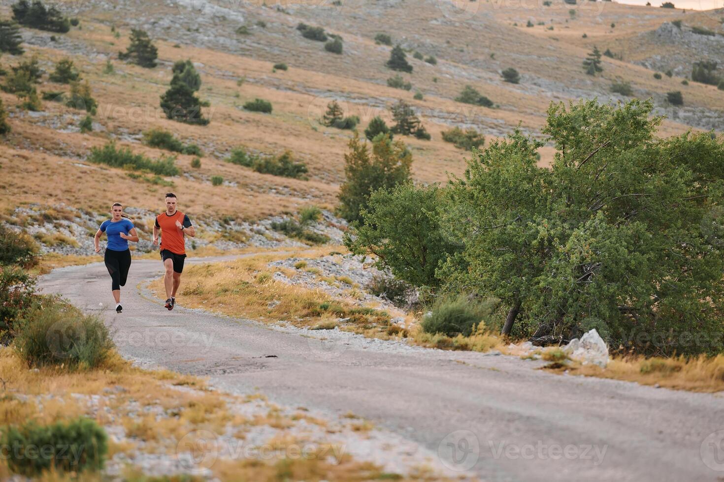 A couple dressed in sportswear runs along a scenic road during an early morning workout, enjoying the fresh air and maintaining a healthy lifestyle photo