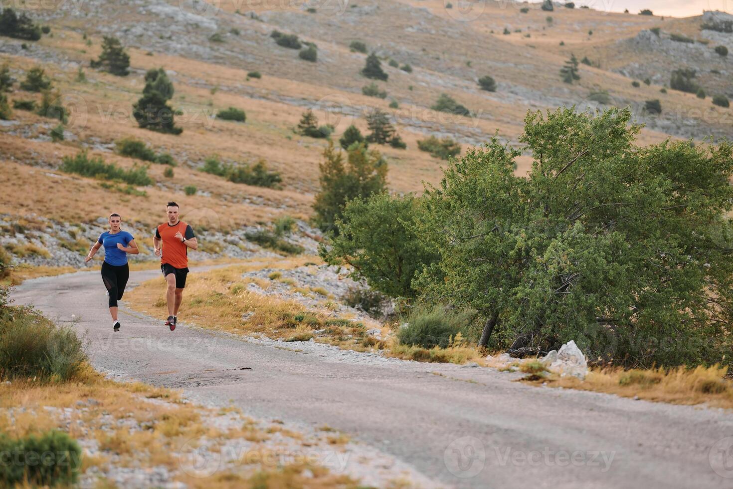 A couple dressed in sportswear runs along a scenic road during an early morning workout, enjoying the fresh air and maintaining a healthy lifestyle photo