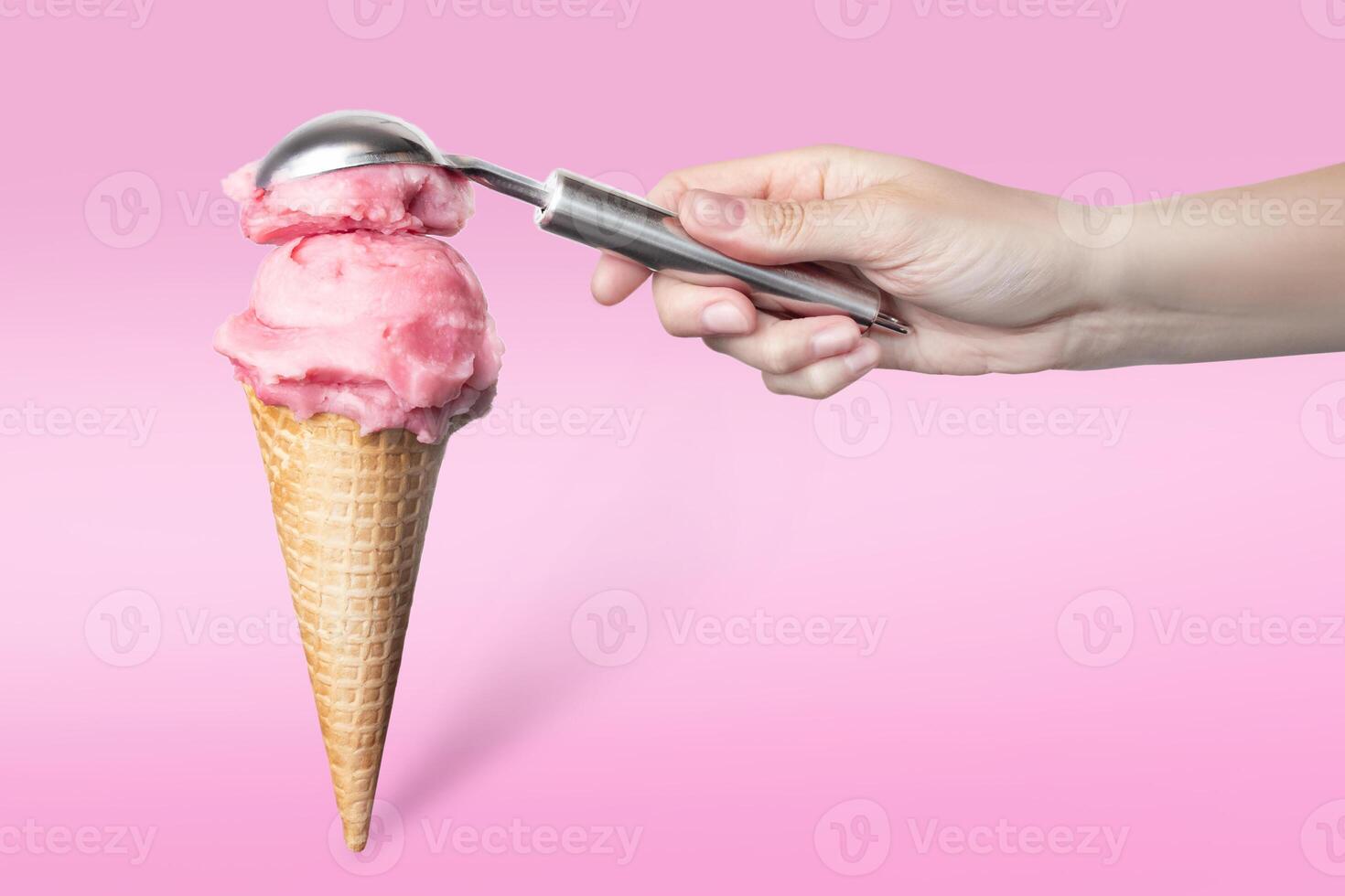 Strawberry ice cream waffle cone on pink background vertical food photo minimalism. Woman's hand puts a scoop of strawberry ice cream