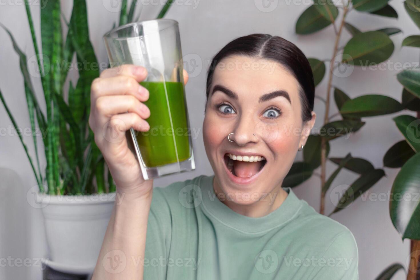 The woman is happy and smiling. Woman drinking green healthy smoothie, drink. She drinks green wheatgrass energy shake. house interior with plants photo