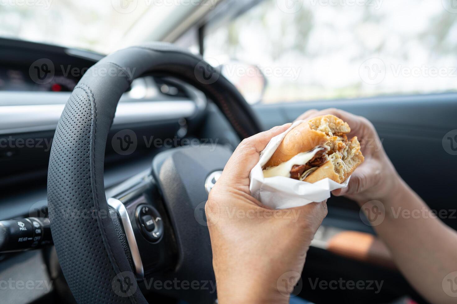 Asian lady holding hamburger and French fries to eat in car, dangerous and risk an accident. photo