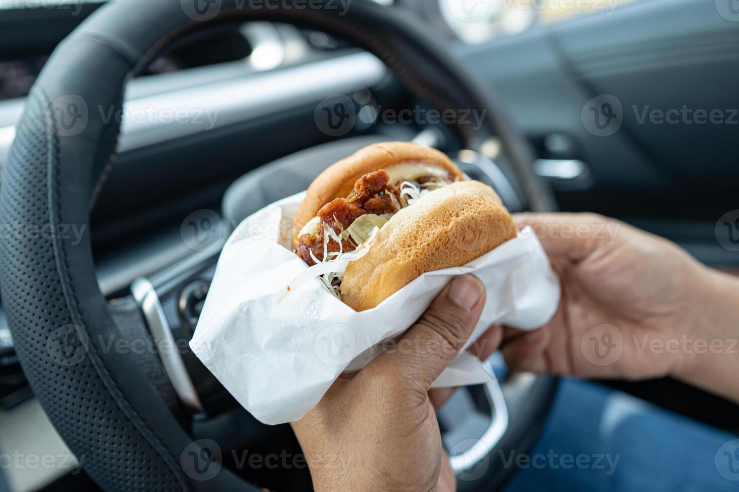 Asian lady holding hamburger to eat in car, dangerous and risk an accident. photo