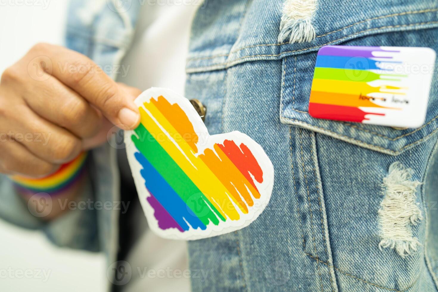 Asian lady wearing rainbow flag wristbands and hold red heart, symbol of LGBT pride month celebrate annual in June social of gay, lesbian, bisexual, transgender, human rights. photo