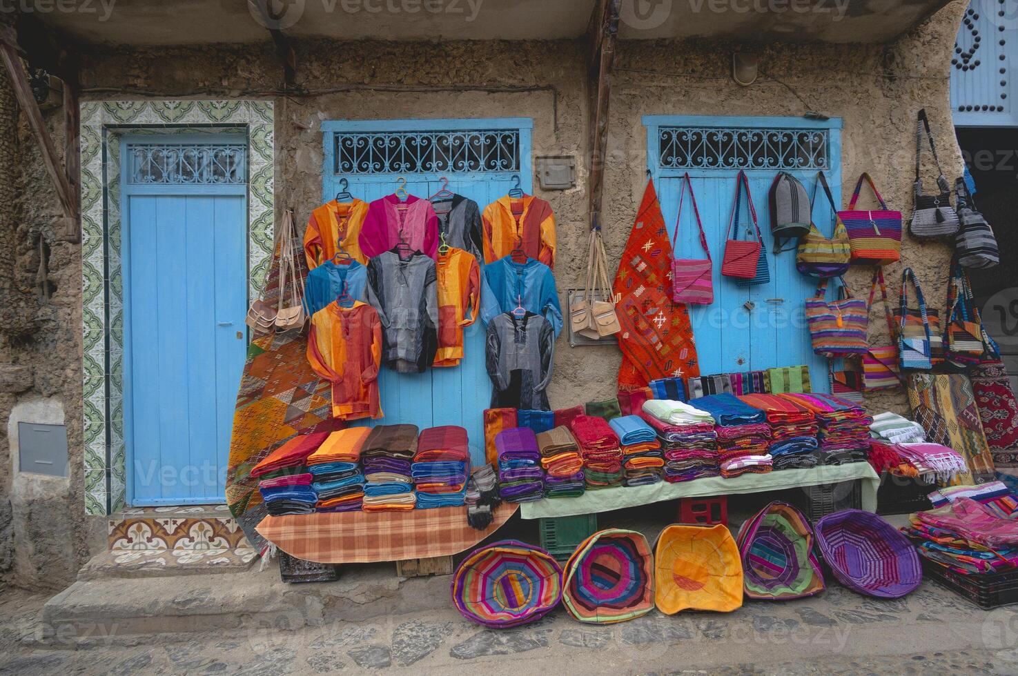 Moroccan handmade crafts, carpets, clothes, bags and other products hanging over the wall on the streets of Chefchaouen Medina, the blue city in Morocco. Variety of souvenirs for sale. photo