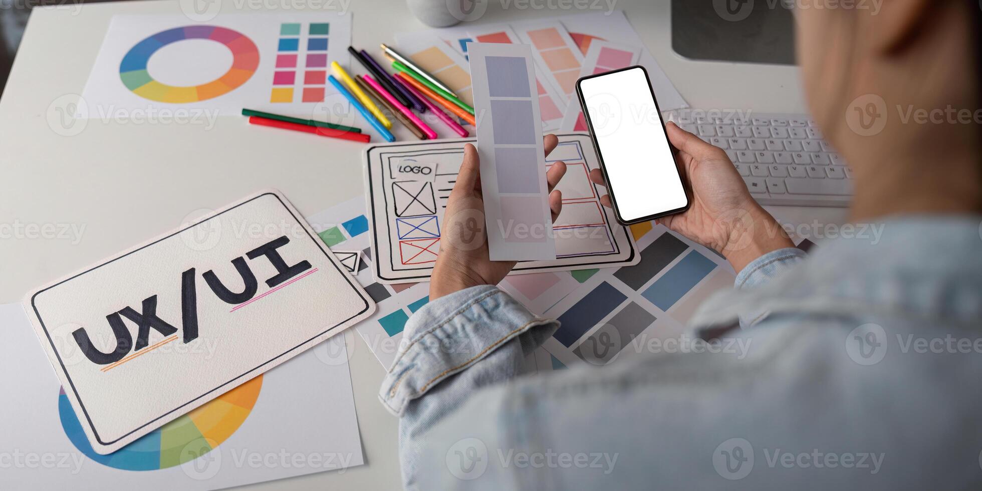 Woman hands holding a smartphone white screen mockup over modern graphic designer office desk photo