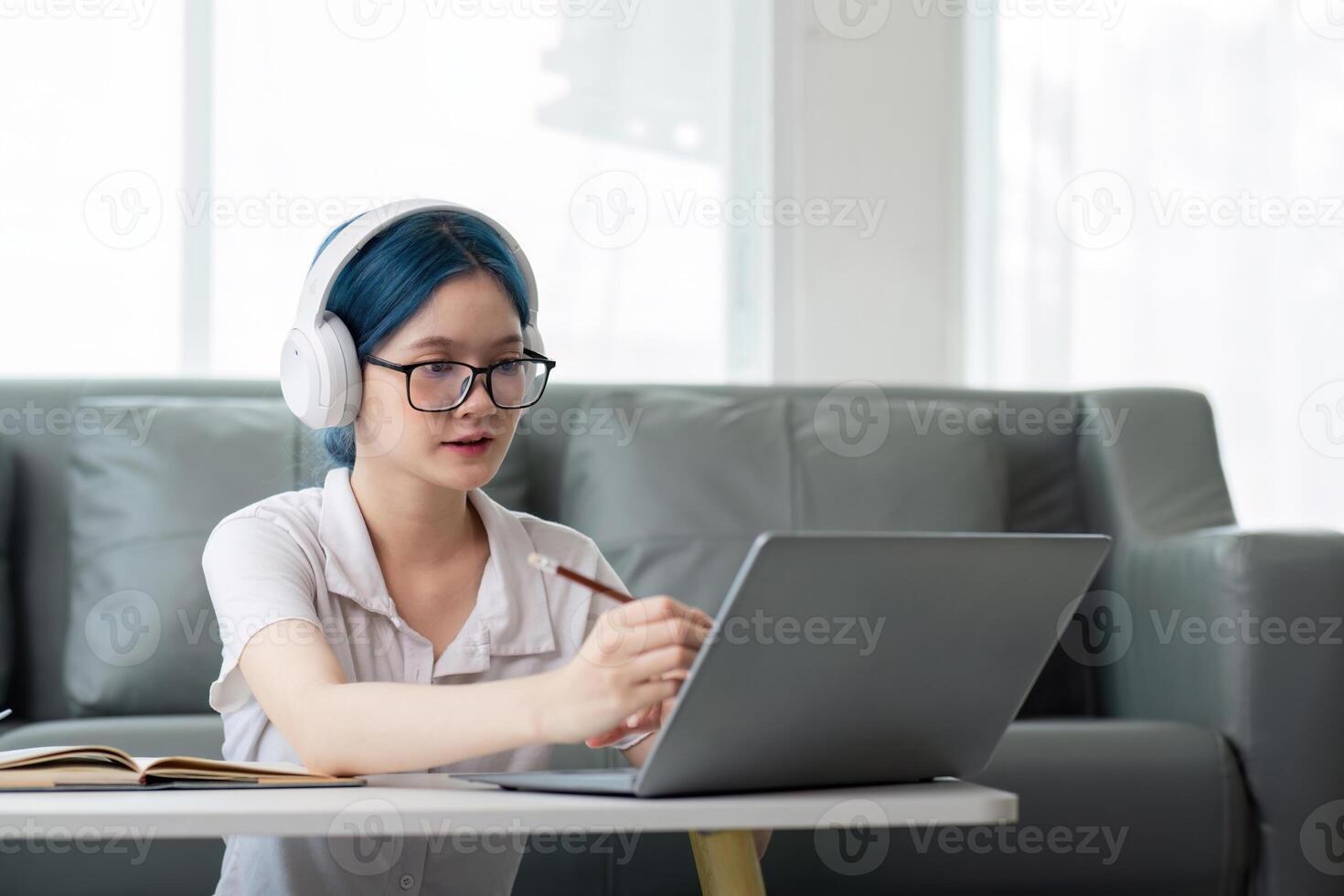 Smiling girl student wear headphone study online with teacher, happy young asian woman learn lecture watch webinar write notes look at laptop sit in home, distant education photo