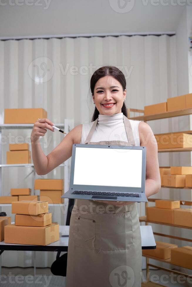 Young business woman asian working online ecommerce shopping at her shop. Young woman sell prepare parcel box of product for deliver to customer. Online selling and mockup using laptop photo