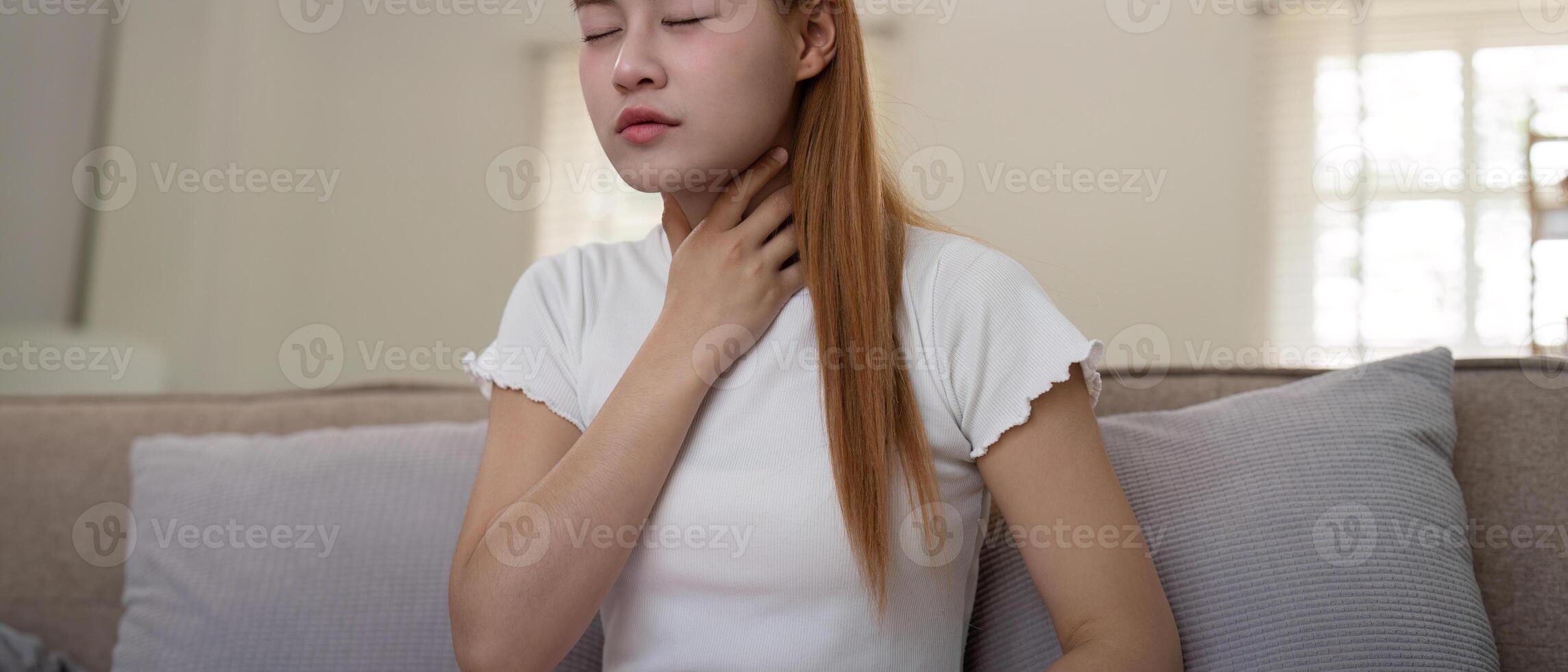 Young woman experiencing throat pain while sitting on a sofa at home photo