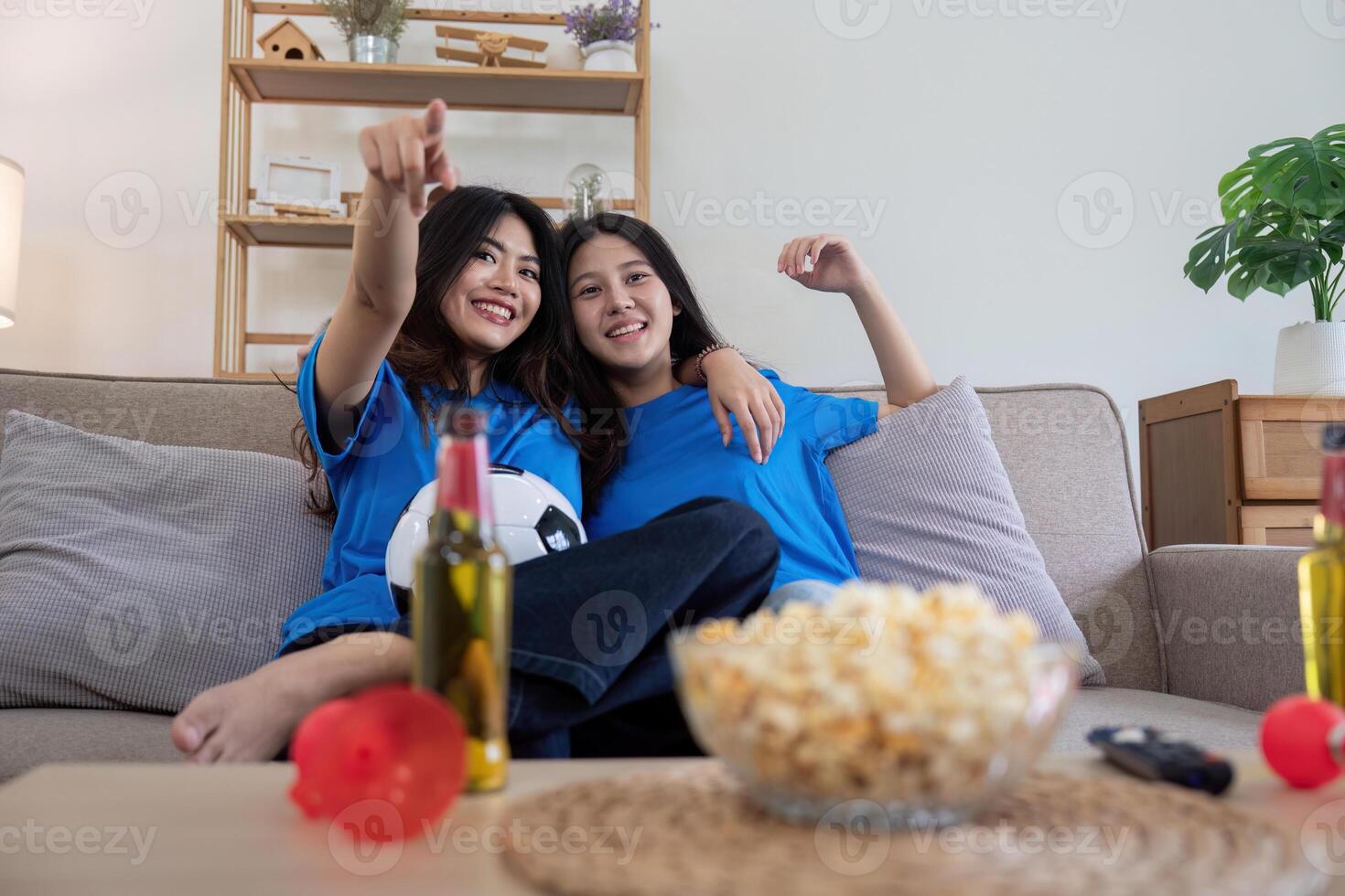 Friends cheering while watching a football game at home. Two women enjoying a sports match on TV with popcorn and drinks photo