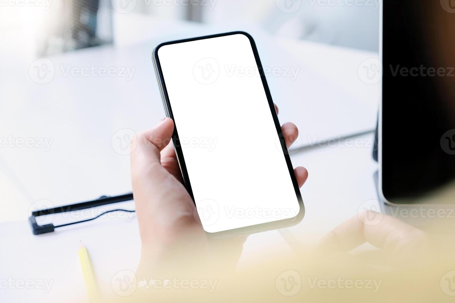 Woman hand holding smartphone on workplace. Blank screen mobile phone for graphic display montage photo