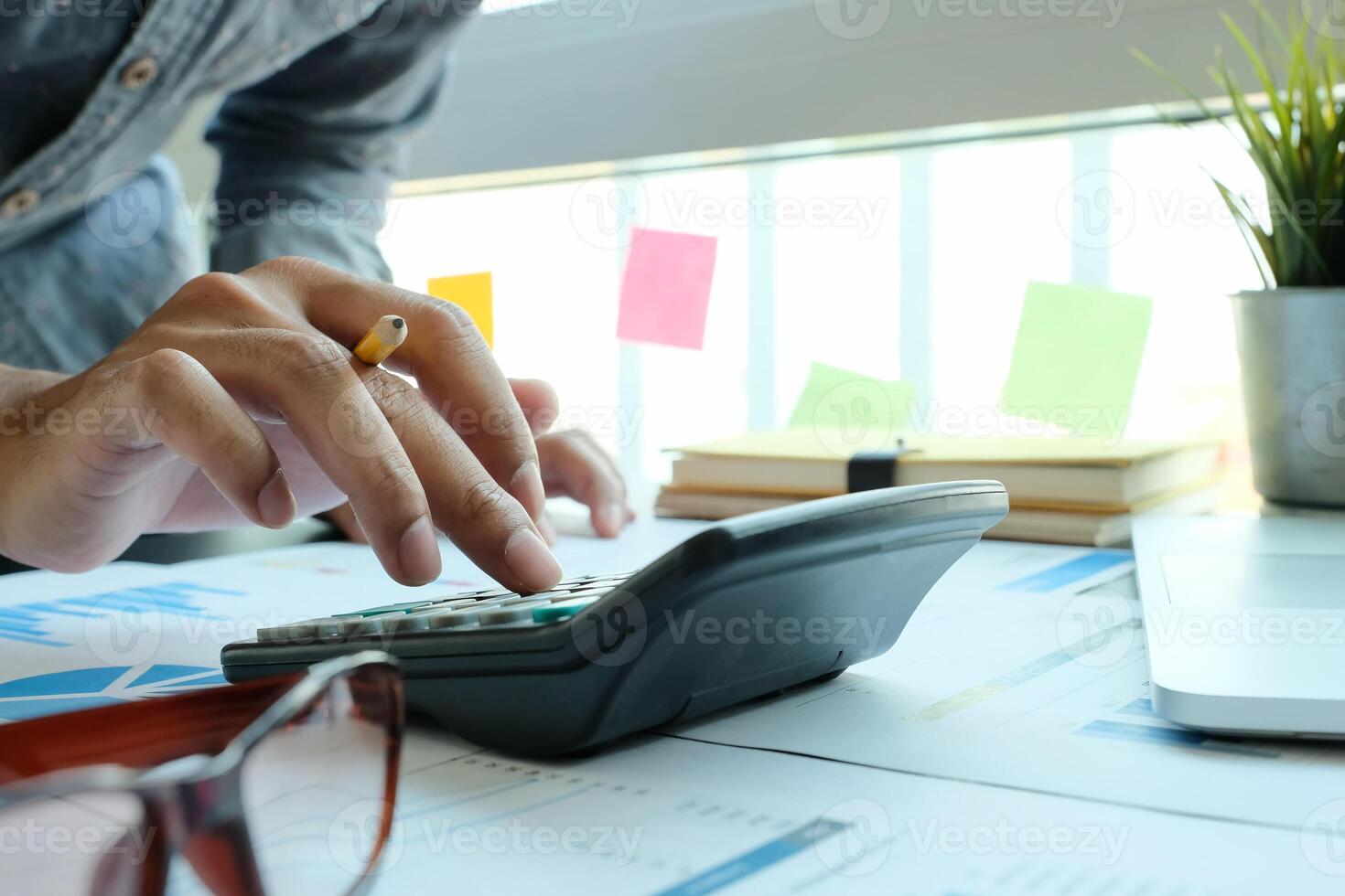 Close up of businessman or accountant hand holding pencil working on calculator to calculate financial data report, photo