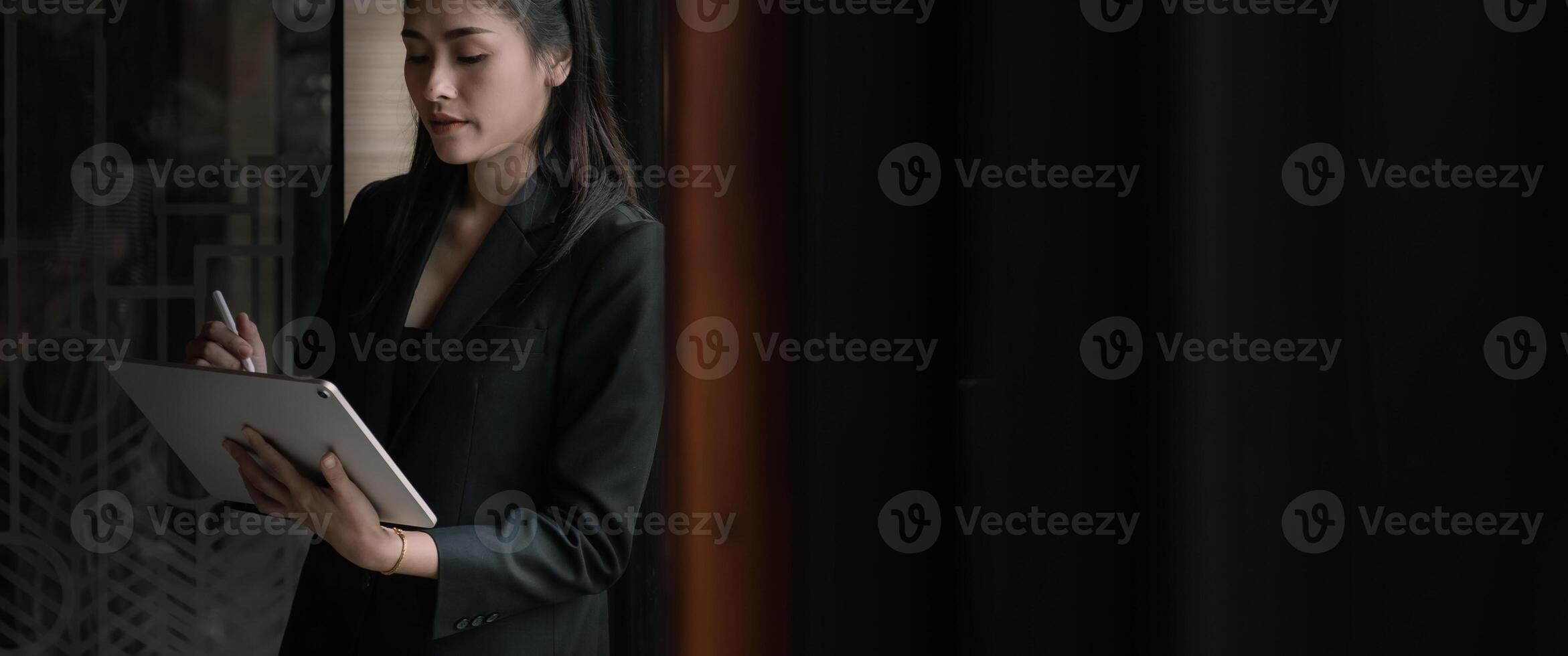 Attractive business asian woman using a digital tablet while standing in front of windows in an office building photo