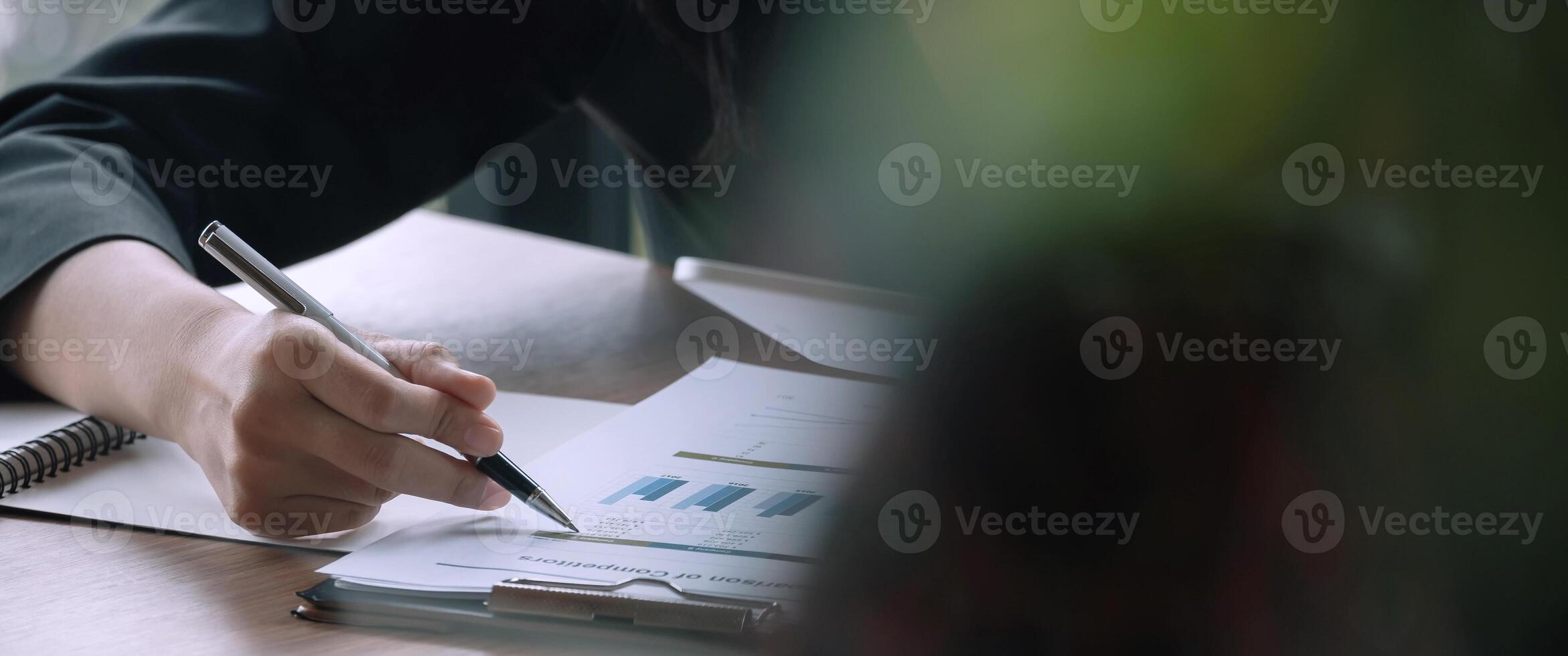 Close up businessman pen pointing turnover with graph chart report and use laptop computer for analysis data photo