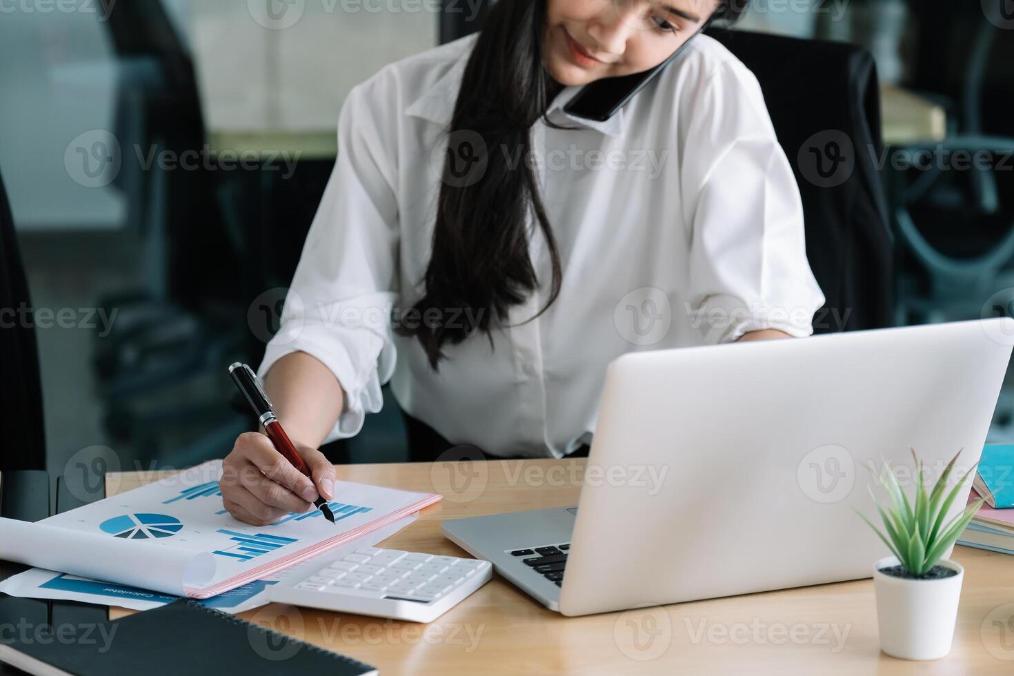 Young accountant hand holding smartphone to call marketing consultants and using laptop computer to analyze sales growth in the global workplace market. accounting concept photo