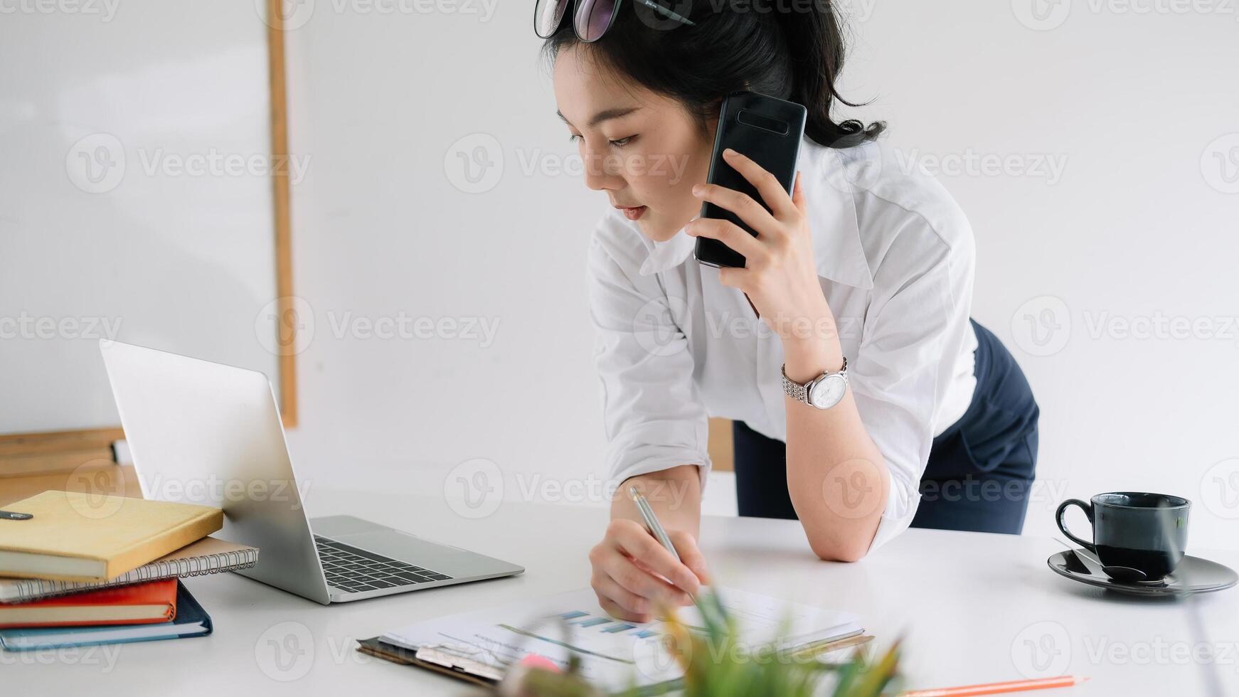 Young female entrepreneur working laptop computer and talking mobile phone photo