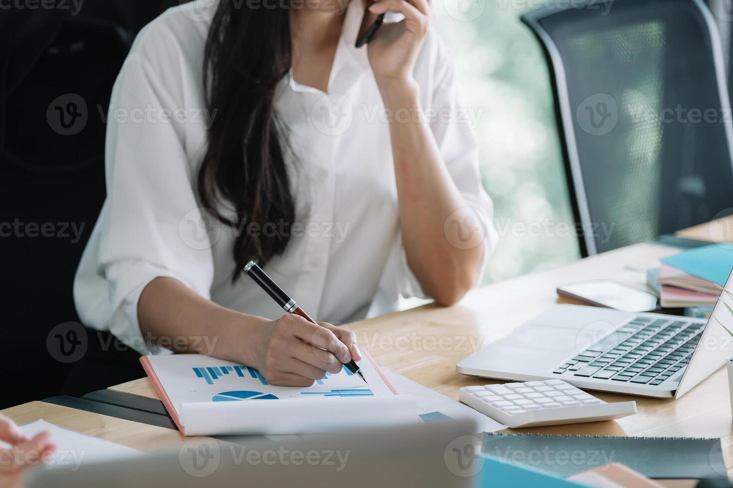 Young accountant hand holding smartphone to call marketing consultants and using laptop computer to analyze sales growth in the global workplace market. accounting concept photo